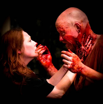 Lady Macbeth, hair down, blood on hter chin and nose, places her bloody hands around Macbeth's neck, as he, holding bloody hands up, looks into her face.