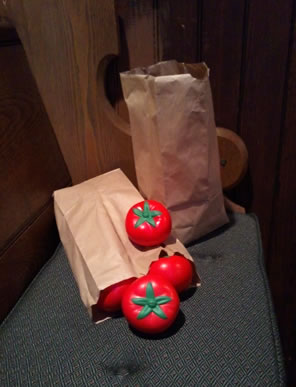 Two bags of foam tomatoes on a cushioned church pew