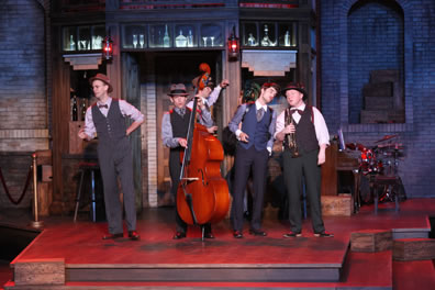 On the three-step platform of the speakeasy set, the musicians in vests and bowties sing, Dull with his standup bass, Costard holding his trumpet