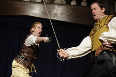 Mercutio in leather jerkin thrusts his sword with ayell as Tybalt in yellow fest parries Mercutio's thrust with his sword while his left hand sits bent at the hip.