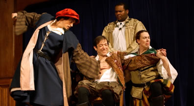 Shylock in blue renaissance robe with brown striped sleeves and red cap holds back the knife with hir right hand and has his left palm on Antonio's bare breast; Antonio sitting, wincing at what's coming, holding the hands of Salarino, while the Duke of Venice in gold robes holds Antonio's shoulder