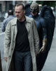 Keaten in black sweatshirt, blue jeans, gray trenchcoat walking down the street (tree on his right, gate on his left) with Birdman in black armor, gold gloves and hood/mask, and large black wings behind him