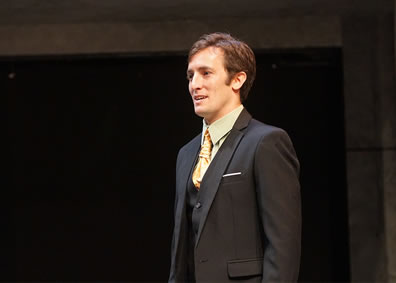 Cassius in three pice suit, dark gray jacket and vest, light green shirt, gold multiknotted tie, sliver of white handkerchief in breast pocket