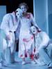 All in white, Lavinia in blood-stained dress and bloody stumps stands in the center with one arm hugging the neck of Titus and the other on the shoulder of Marcus as they grieve over her mutilation. Titus is wearing a white commedia mask and a soldiers cap, Marcus is in white face