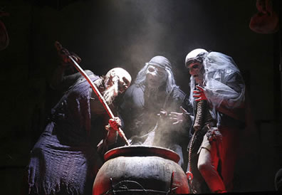 Weird sisters under a spotlight stir their potion in the cauldron