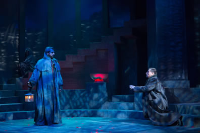 Caesar in a long overcoat and a beard holds the lanter, Brutus, also in overcoat, kneels and reaches toward the ghost. The glowing bowl is in the center of the picture, and behind Caesar barely visible in the shadow-patterend light is the Soothsayer sitting on the steps rising at the back of the stage.