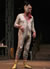 Malvolio in tattered long johns, skull cap with horns, turkey wattle around his chin, and yellow stockings on his feet