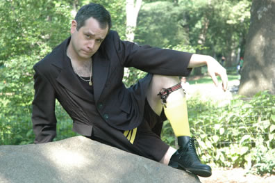 Malvolio lounges on a rock wearing a classic bathing suit, with yellow stockings and garter, underneath his stewards coat, and he still has his chain on