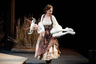 Audrey in country dress carries a woman dressed as a white goat across her back.