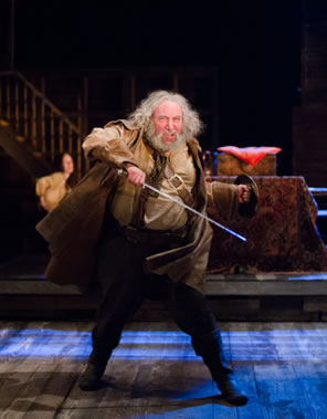 Falstaff swings his hacked sword arund, the motion obvious in his cloak as he stands leg separated, wearing a small shield in his left hand and an excited in his expression. A tavern wench listens in the background.