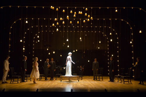 Hermione looking like a statue on a platform on wheels amid layers of lights and lamps hanging down from the ceiling. The rest of the cast stand around the perimeter next to chairs