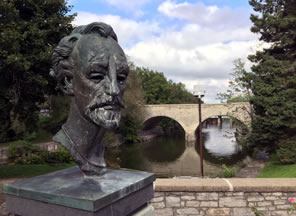 Photo of a bust of Shakespeare with river going under bridge in background