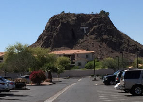 Photo of a rock-cliff stump of a hill, a white "T" on its face, beyond a parking lot and apartments