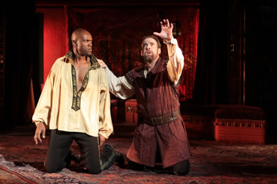 Othello and Iago kneeling, Iago with one hand raise, the other on Othello's shoulder