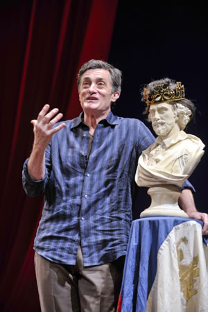 Roger Rees talks while standing next to a bust of Shakespeare wearing a crown
